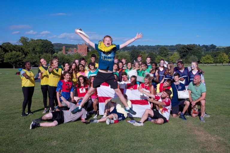 Young learners and staff celebrate together on a sunny sports field during an English summer camp.