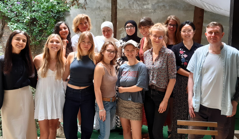 Adult learners and teachers pose in a leafy courtyard during an international course in Budapest.
