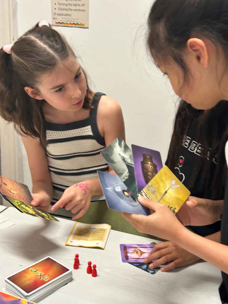 Two young learners discuss illustrated cards during a collaborative classroom language activity.