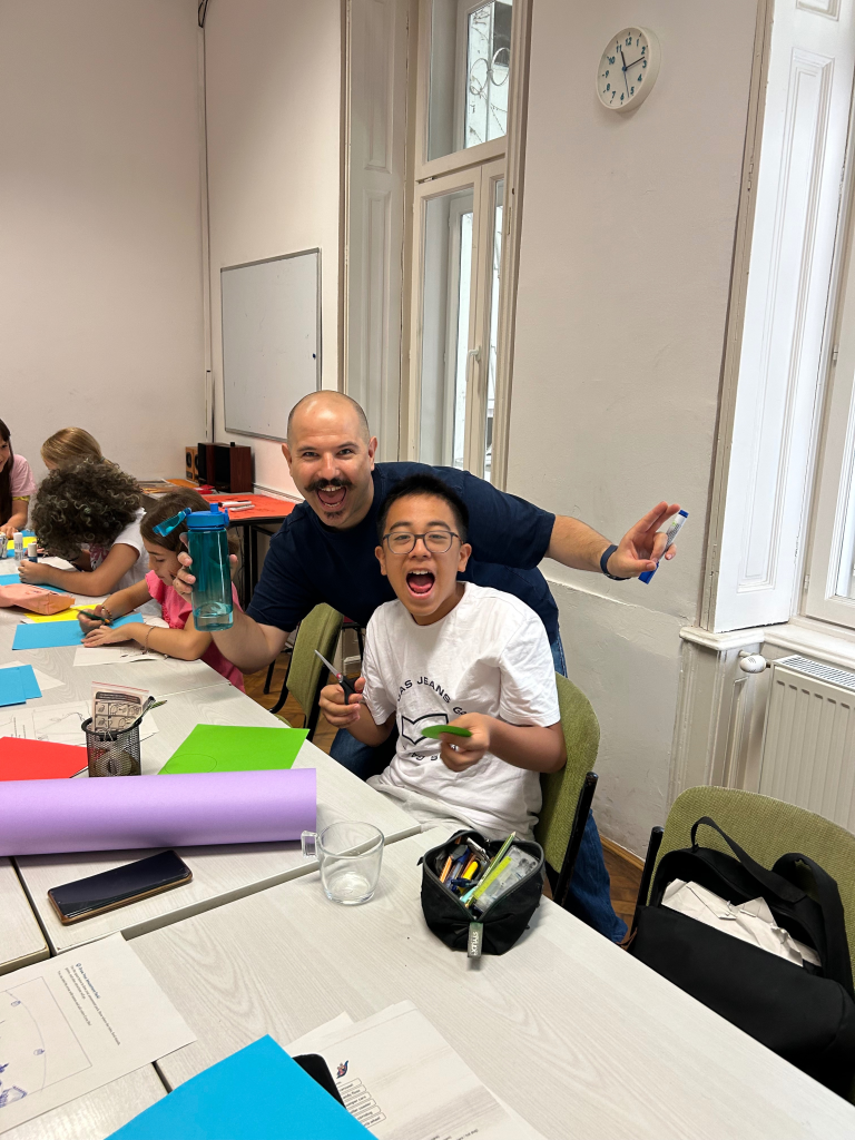 A teacher and young learner smile during a creative classroom activity with colourful paper.